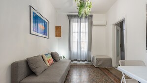 A living room with a sofa, a small table, a window with curtains, and a hanging plant. - 'Fiorelli 17 - Bivano Green Leaves' Apartment with Balcony, Wi-Fi and Air Conditioning (Palermo)