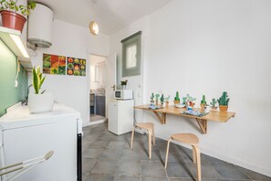 A compact kitchen with a refrigerator, microwave, and a small dining table with chairs. There are potted plants and a wall-mounted shelf. - 'Fiorelli 17 - Bivano Green Leaves' Apartment with Balcony, Wi-Fi and Air Conditioning (Palermo)