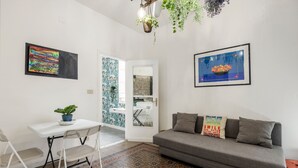 A room with a white desk, a grey sofa, a patterned rug, and two wall-mounted artworks. - 'Fiorelli 17 - Bivano Green Leaves' Apartment with Balcony, Wi-Fi and Air Conditioning (Palermo)