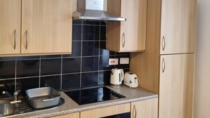 A kitchen with wooden cabinets, a black tiled backsplash, a stainless steel range hood, a black oven, a sink, and a countertop with a kettle and toaster.