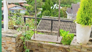 A balcony with a swing, potted plants, and a view of a residential area. - SWEET VALLEY HOMESTAY (Xuan Huong - Da Lat)