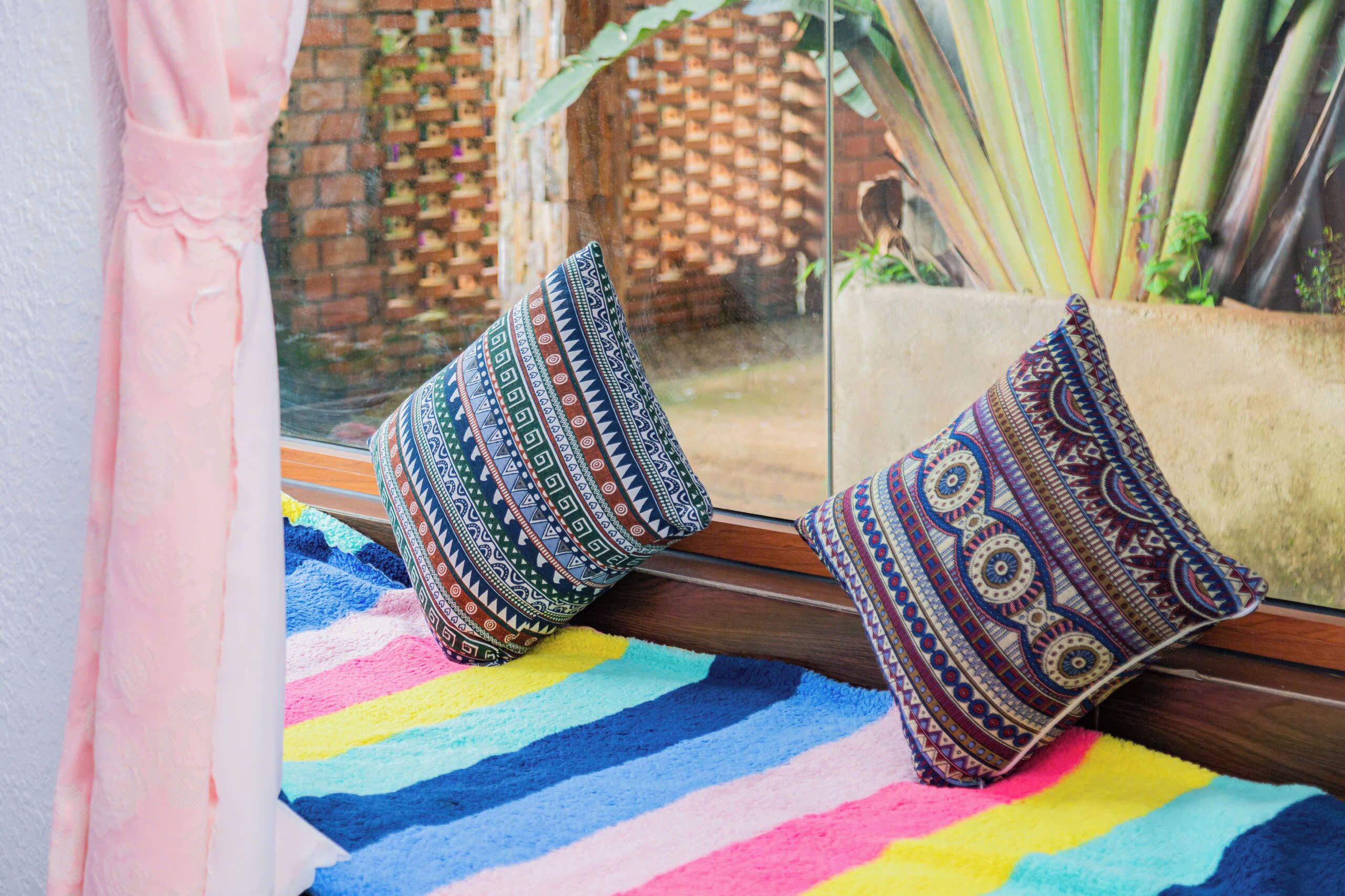 A window with two patterned cushions on a colorful striped rug.