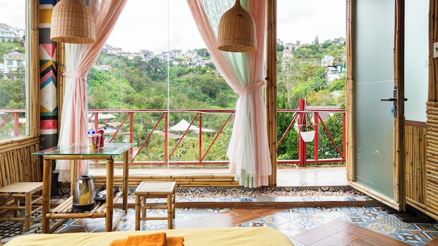 A room with a balcony, a bed, a table, and a hanging light fixture. - SWEET VALLEY HOMESTAY (Xuan Huong - Da Lat)