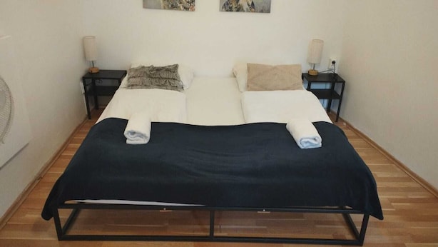 Een tweepersoonsbed met een zwart frame, twee nachtkastjes met lampen en een houten vloer.