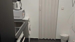 Een kleine keuken met een magnetron, een koffiezetapparaat en een wasmachine.