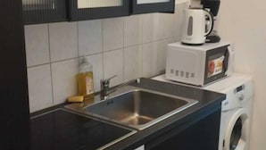 Een kleine keuken met een spoelbak, een magnetron, een koffiezetapparaat en een wasmachine.