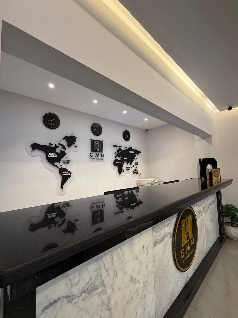 A reception desk with a marble top and a logo. There are wall clocks and a world map.