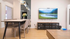A modern living room with a dining area, a flat-screen TV mounted on the wall, and a wooden coffee table. - Tyms Family APT Spacious 3BR for Groups & Families  (Shanghai)