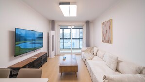 A modern living room with a flat-screen TV, a wooden coffee table, a sofa, and a large window with a city view. - Tyms Family APT Spacious 3BR for Groups & Families  (Shanghai)