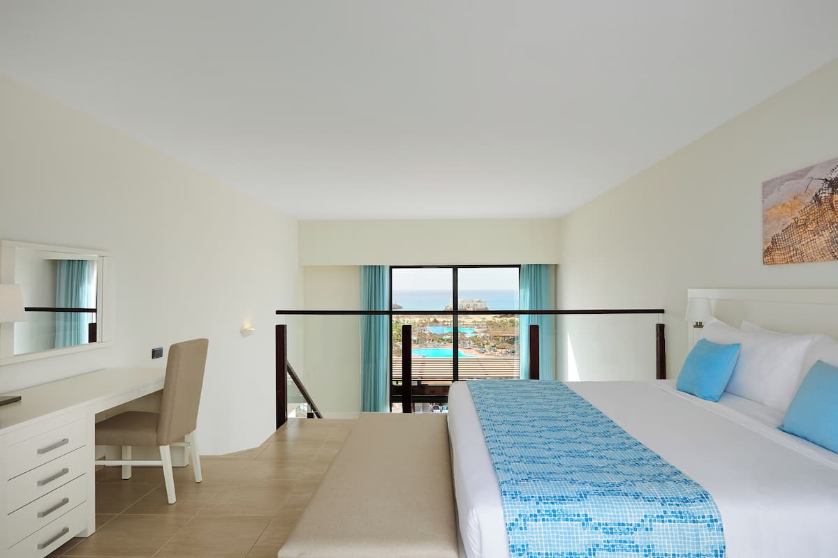 A hotel room with a bed, a desk, a chair, and a view of a pool and resort.