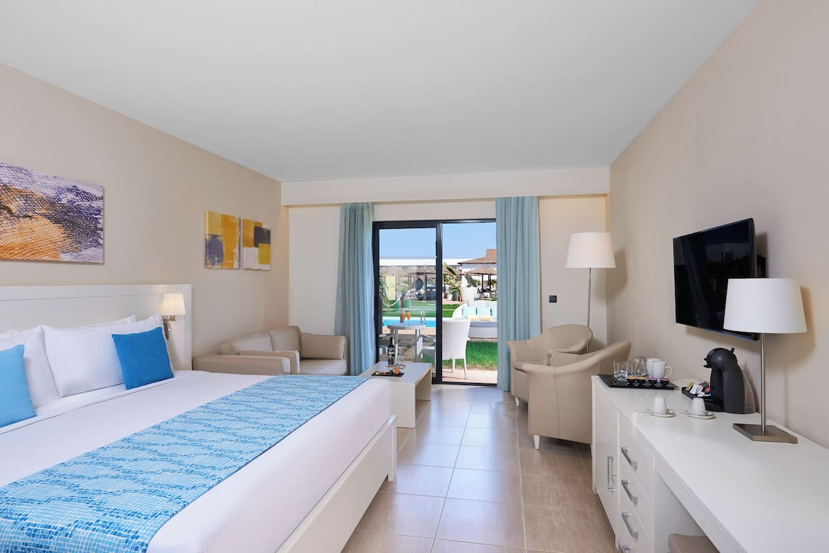 A hotel room with a bed, a desk, a TV, and a view of the pool.