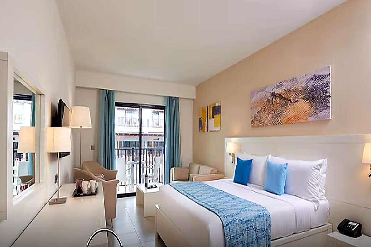 Une chambre d’hôtel avec un lit, un bureau, une chaise, une fenêtre avec des rideaux et un tableau au mur.