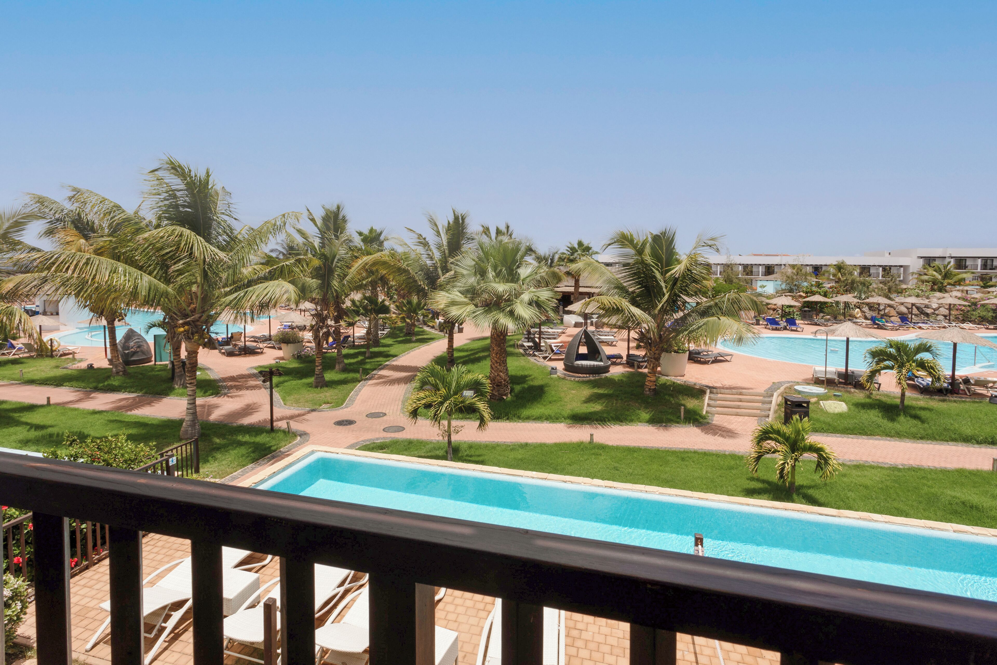 Ein Poolbereich eines Resorts mit Palmen, Liegestühlen und einem Gebäude im Hintergrund.
