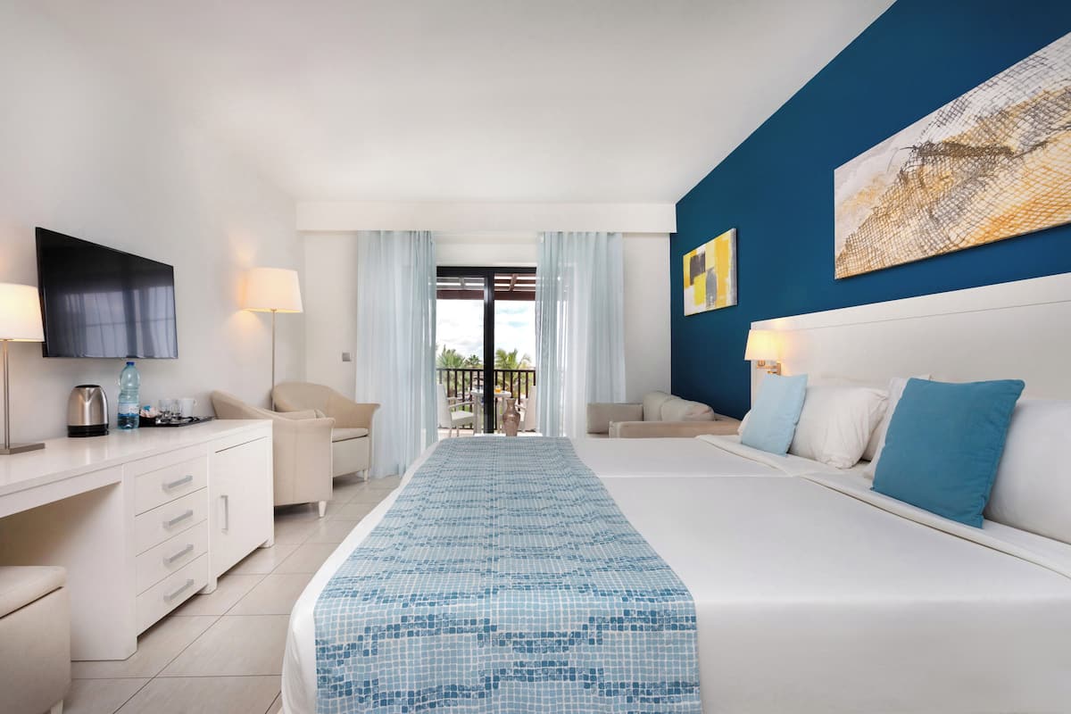 A hotel room with a bed, a desk, a TV, and a balcony with a view.