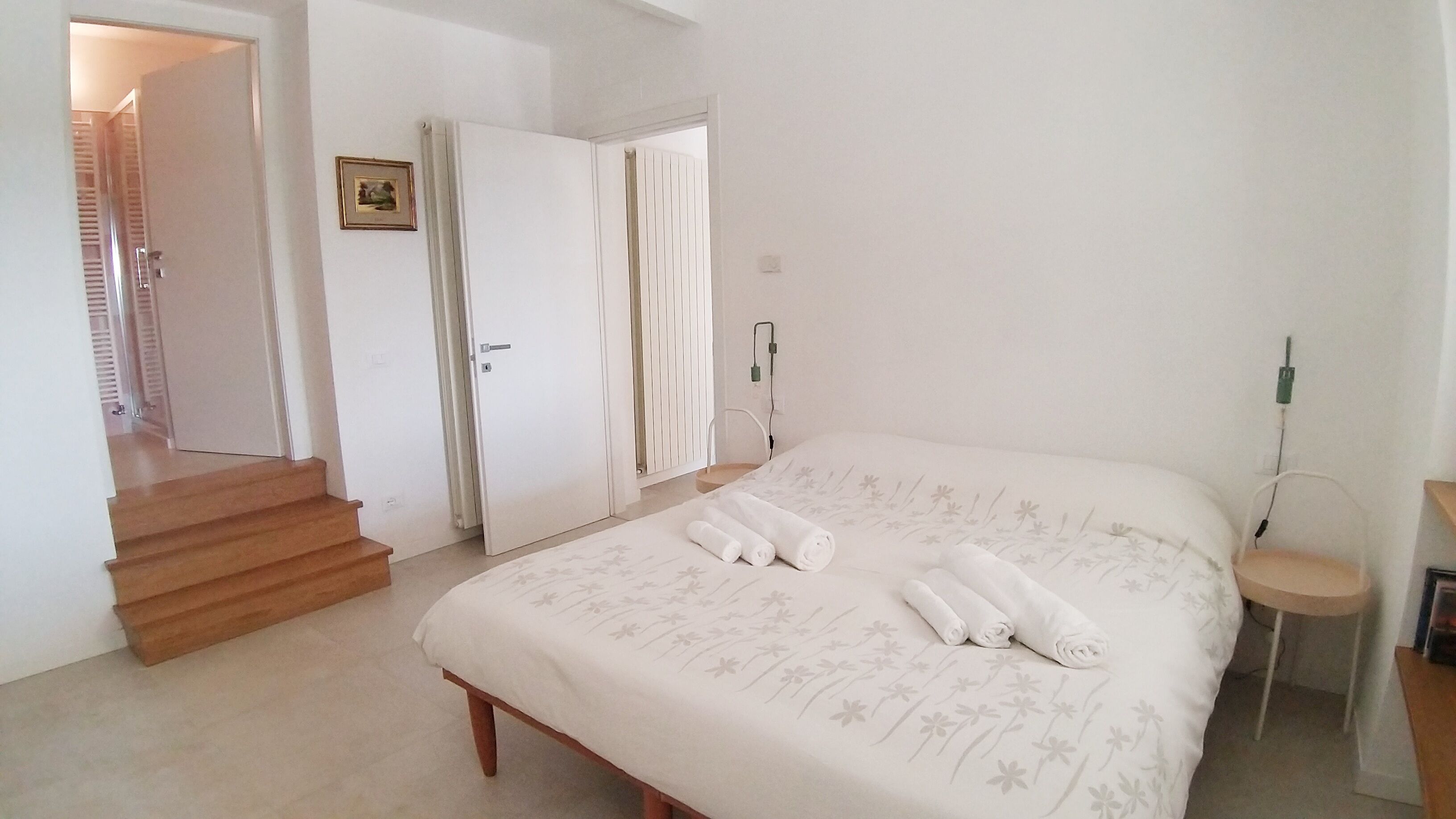 A bedroom with a bed, a wooden staircase, and a door leading to another room.