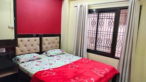Une chambre à coucher avec un lit, un mur rouge, une fenêtre avec des barreaux en métal et un plancher en bois.