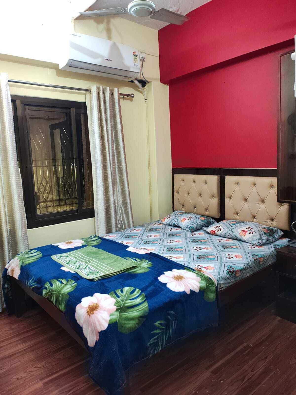 Un dormitorio con cama, cortinas, un equipo de aire acondicionado y una pared roja.