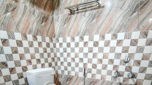 Une salle de bain avec un sol en marbre, des toilettes blanches, un seau rose et un carrelage mural à motifs à carreaux.