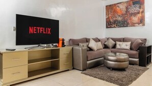 A living room with a flat-screen TV displaying 'NETFLIX', a sofa, a coffee table, and a cabinet.
