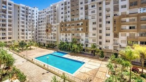 A residential building with multiple balconies, a swimming pool, and surrounding greenery.