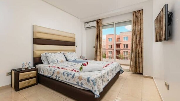A bedroom with a bed, a nightstand, a TV, and a window with curtains.