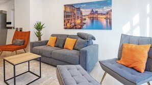 Un salon moderne avec un canapé gris, des coussins orange, une table basse en bois et un fauteuil gris.