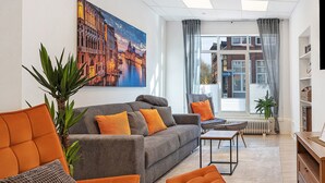 Un salon moderne comprenant un canapé, des fauteuils, une table basse et un grand tableau représentant un paysage urbain.