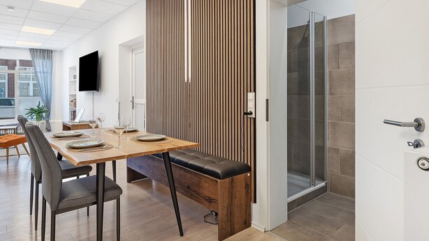 Un intérieur moderne avec un séparateur en bois, un banc, une table à manger avec des chaises et un espace douche.