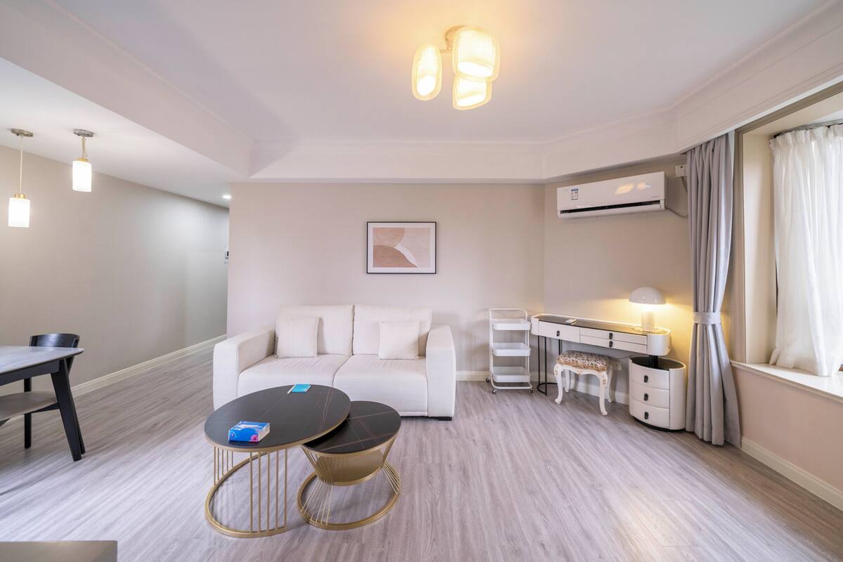 A modern living room with a sofa, a dining table, a coffee table, and a desk with a lamp.