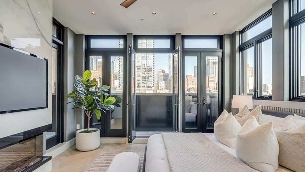 A modern bedroom with a large bed, a potted plant, and a city view through the windows. - Where Rock & Roll Royalty Crash - Hot Tub & More (Philadelphia)