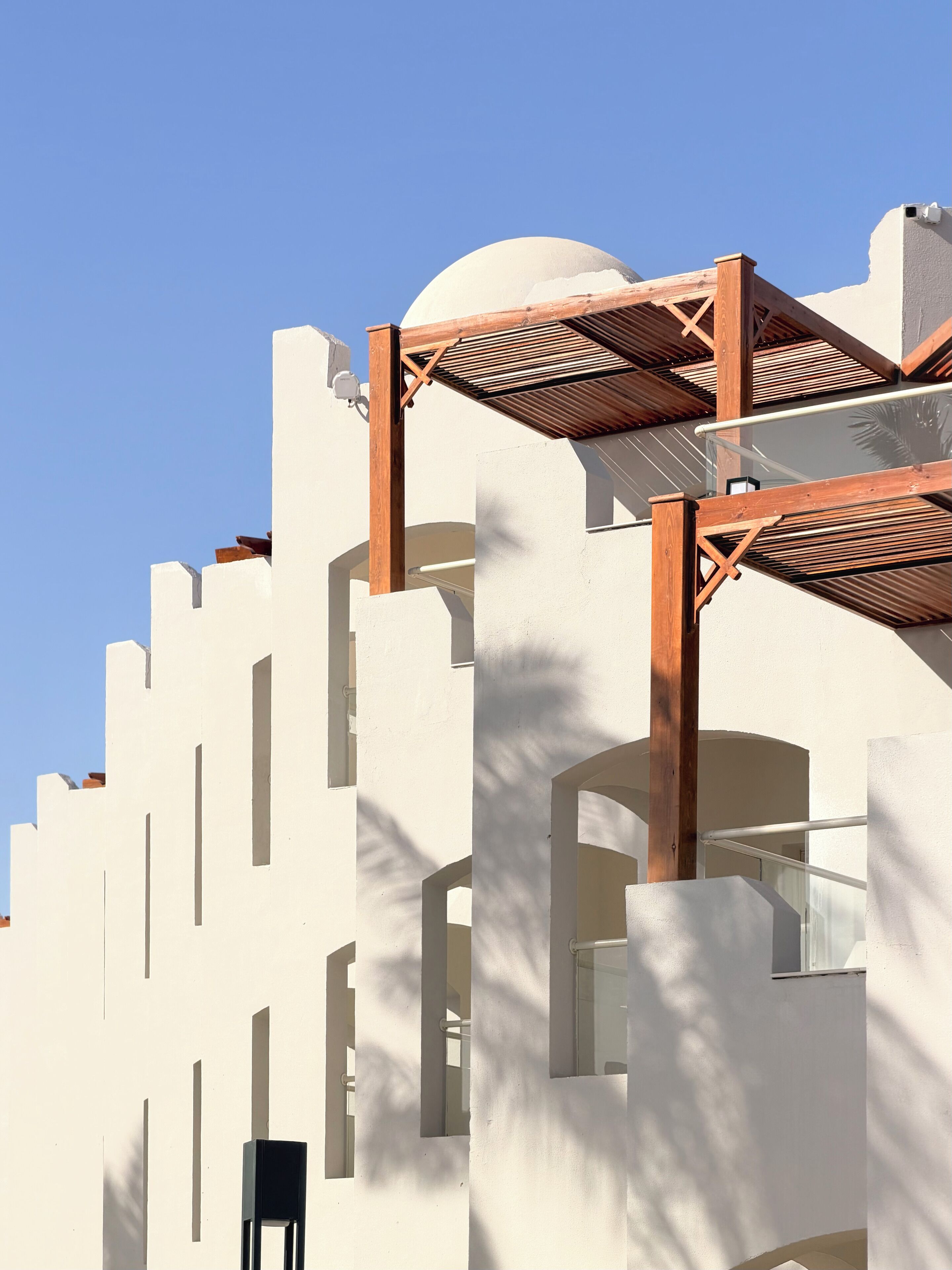 Un edificio moderno con fachada blanca, pérgola de madera y múltiples ventanas.