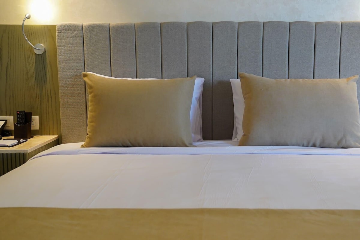 Une chambre d’hôtel avec un grand lit, deux oreillers, une table de chevet avec une lampe et un luminaire fixé au mur.