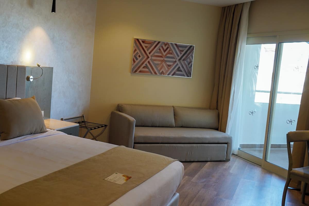 Une chambre d’hôtel avec un lit, un canapé, une petite table et une œuvre d’art accrochée au mur.