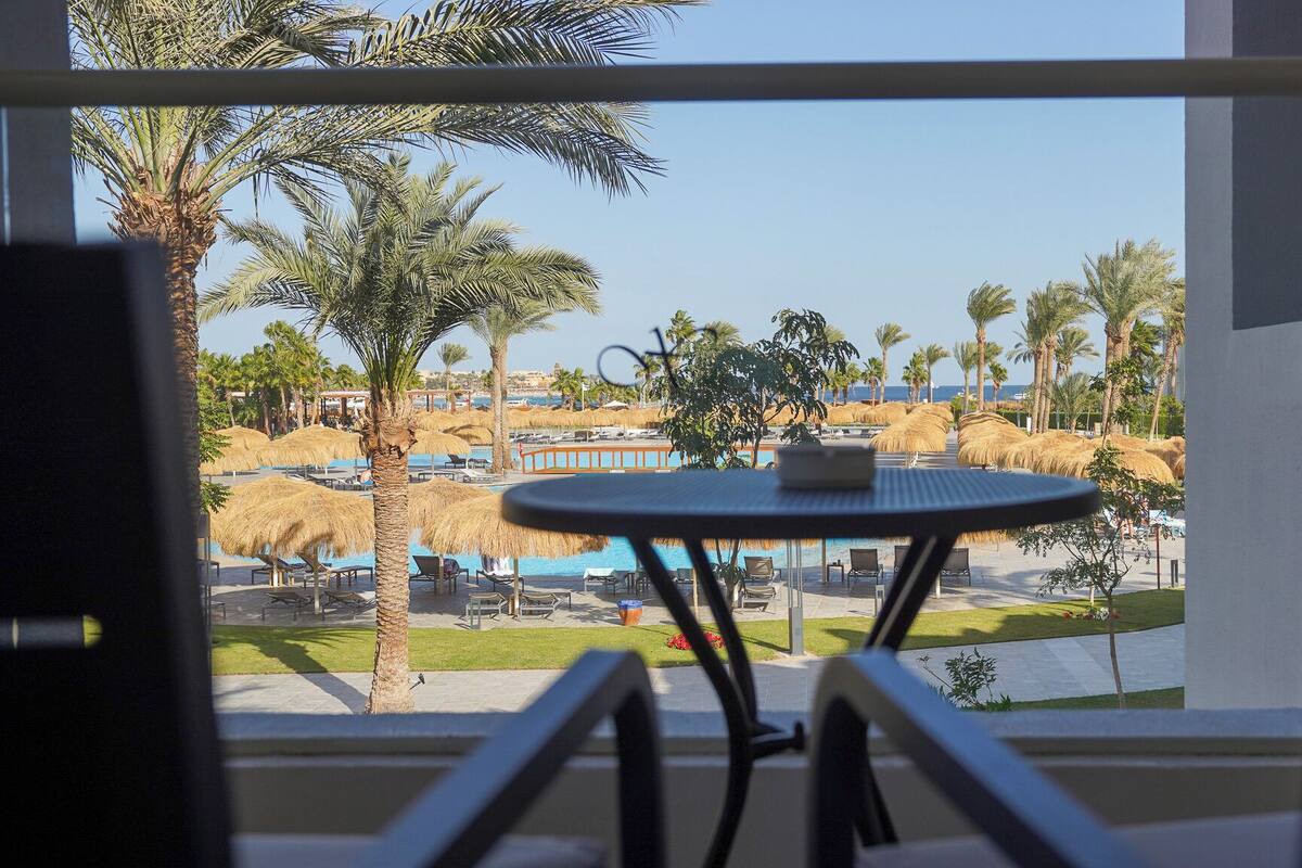 Un balcon avec vue sur une piscine, des palmiers et une plage.