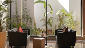 Una hall moderna con due divani neri, un tavolino da caffè e ampie finestre che si affacciano su un giardino ricco di piante.
