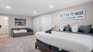 A bedroom with a large bed, a bedside table, a nightstand, a wall-mounted artwork, and a door leading to a bathroom.