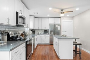 A modern kitchen with white cabinetry, stainless steel appliances, and a wooden floor.
