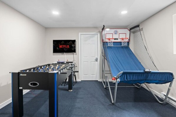 A room with a foosball table, a TV screen displaying Netflix, and a small basketball hoop.