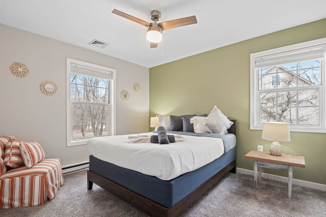 A bedroom with a bed, a chair, a nightstand, a lamp, and a ceiling fan.