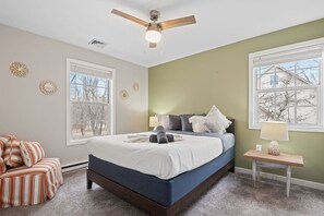 A bedroom with a bed, a chair, a nightstand, a lamp, and a ceiling fan.
