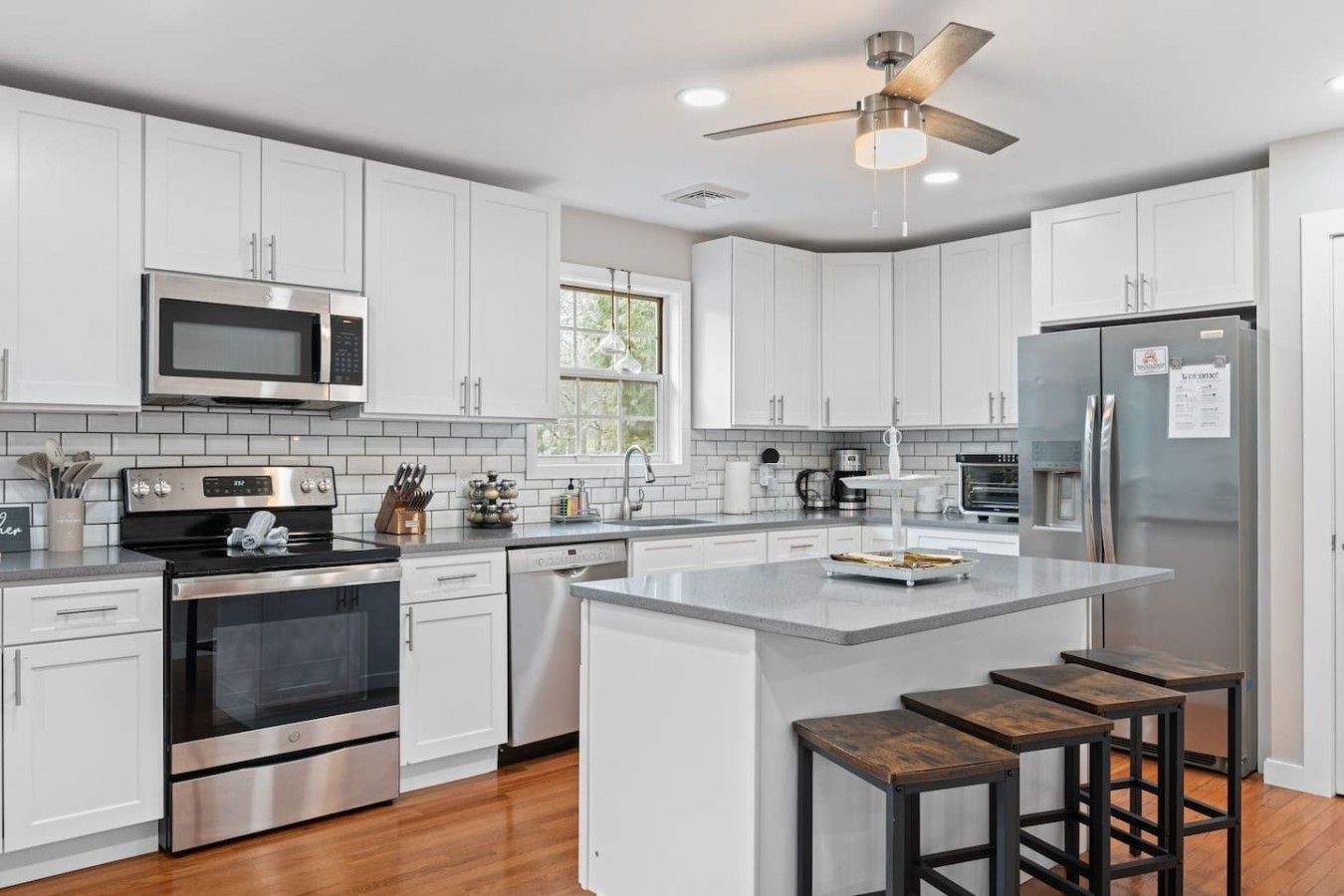 A modern kitchen with white cabinets, stainless steel appliances, and a central island with stools.