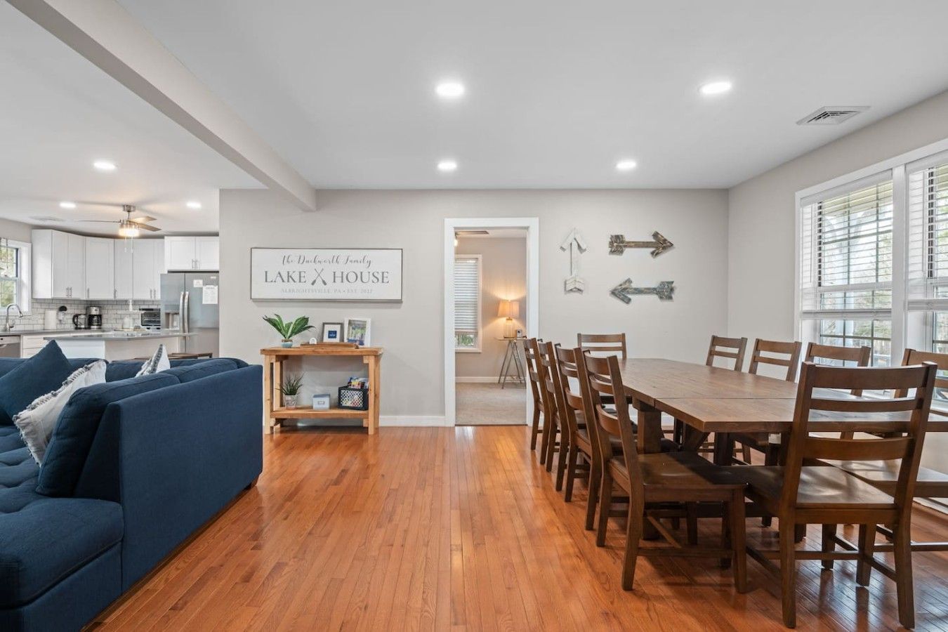 A modern kitchen with white cabinets, a dining area with a wooden table and chairs, and a living room with a blue sofa.