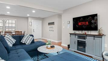 A living room with a blue sofa, a coffee table, and a TV displaying the Netflix logo.