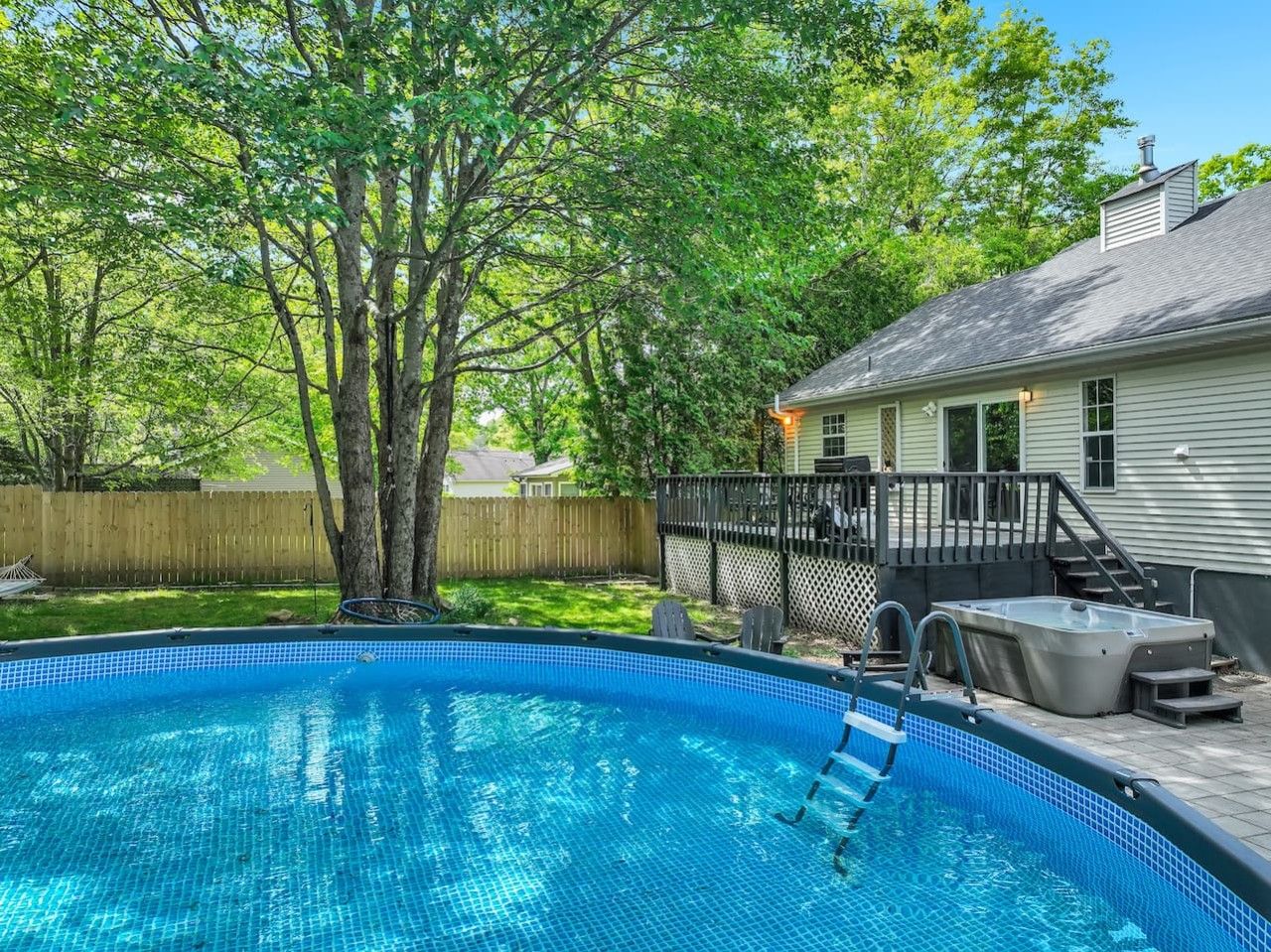 A backyard with a swimming pool, a hot tub, and a covered patio area.