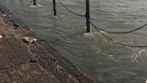 A river with a brick walkway and wooden posts with chains. - Hotel New Pratap (Haridwar)
