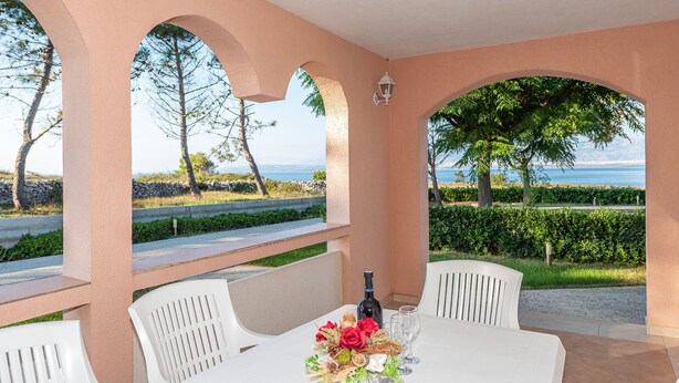 A table set with white chairs and a bottle of wine, overlooking a scenic view of the sea and greenery. - Beachside Holiday Home Marija (Lozice)