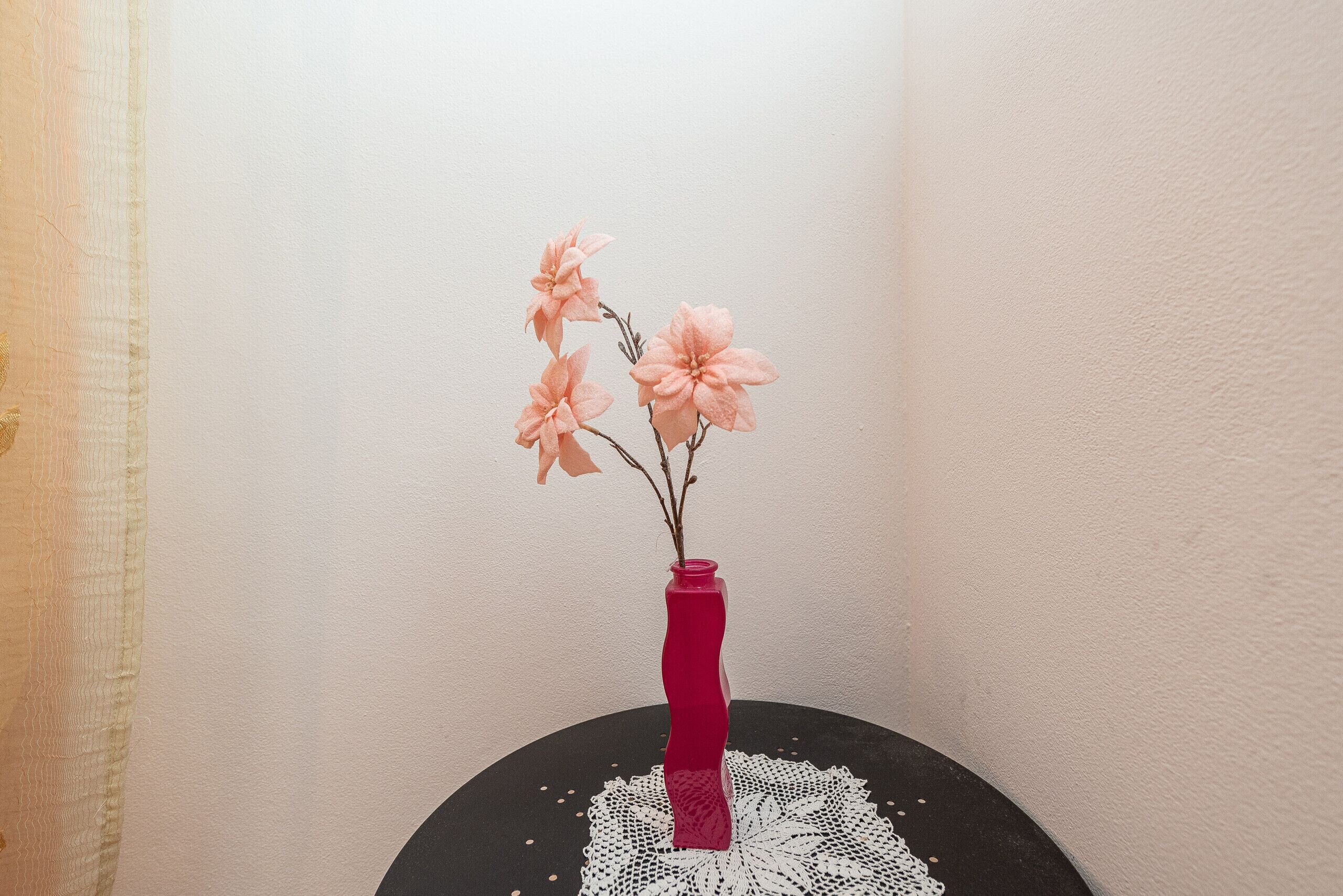 A pink vase with flowers on a black table with a white lace doily.