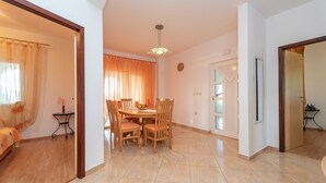 A dining area with a round table and chairs, a small side table with a vase, and a window with curtains. - Beachside Holiday Home Marija (Lozice)