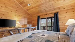 Een houten kamer met een bed, een televisie, een bureau en een raam met gordijnen.