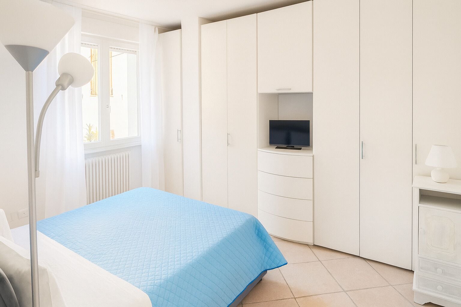 Un dormitorio con una cama, un estante para la televisión, una lámpara y un armario.